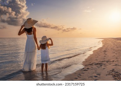 A mother and her daughter in white summer clothing standing on a beautiful beach and enjoying the summer sunset - Powered by Shutterstock