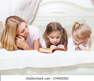 Mother And Her Daughters Reading Bed Time Story Book In Bed