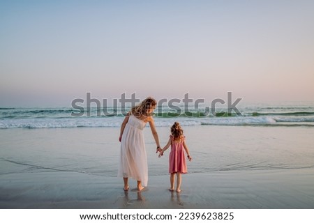 Mother with her little daughter enjoying time at sea, rear view.