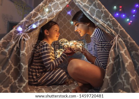 Mother and her little daughter with fairy lights in evening at home