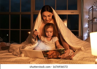 Mother and her little daughter reading bedtime story at home - Shutterstock ID 1676936572