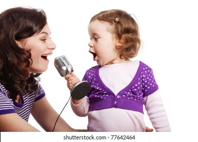 Mother and her little daughter sing into the microphone, looking at each other.