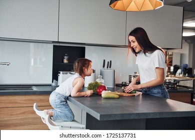 Mother with her little daughter slicing vegetables indoors in kitchen. - Powered by Shutterstock