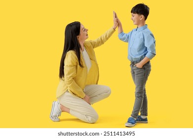 Mother with her little son giving each other high-five on yellow background - Powered by Shutterstock