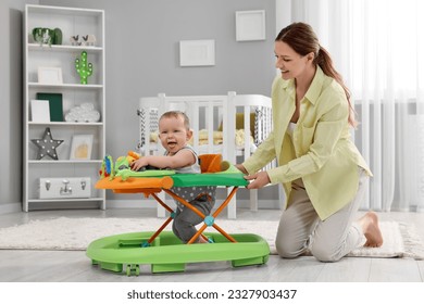 Mother and her little son at home. Cute baby making first steps with toy walker