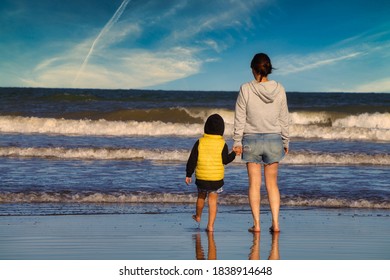 Mother and her son looking to the horizon on a beach. holding hands and standing next to the sea.