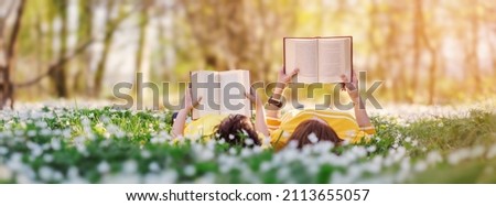 Mother and her son lying down on the beautiful spring field in the sunny park. Concept of the interesting of literature and family leisure.