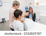 A mother and her son make a payment at the reception of a dental clinic as the receptionist smiles. Concept of dental office payment.