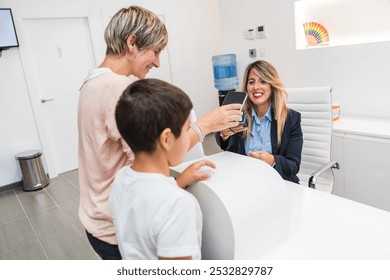 A mother and her son make a payment at the reception of a dental clinic as the receptionist smiles. Concept of dental office payment. - Powered by Shutterstock