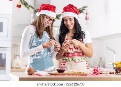 A mother and her teenage daughter dressed in Christmas aprons are making Christmas cookies at home in the kitchen.