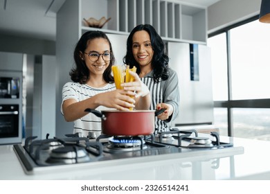 A mother and her teenage daughter joyfully cooking together in the kitchen, sharing laughter and creating a delicious meal - Powered by Shutterstock