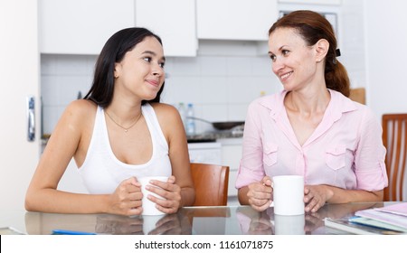 Mother And Her Teenage Daughter Talking At Kitchen Table