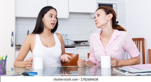 Mother And Her Teenage Daughter Talking At Kitchen Table