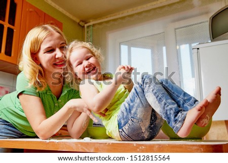 Mother and her three years old blonde daughter are cooking in a kitchen. Pampering with flour and dough on the table. Funny photoshoot of a little girl and an adult woman
