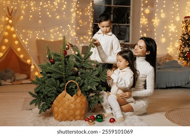 A mother and her two children decorating a small Christmas tree in a cozy, festive room adorned with fairy lights. The children are playfully reaching for ornaments, while the mother watches - Powered by Shutterstock