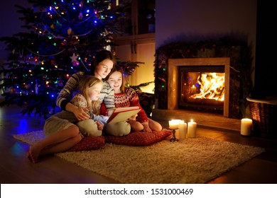 Mother and her two cute young daughters using a tablet pc at home by a fireplace in warm and cozy living room on Christmas eve. Winter evening at home with family and kids. - Powered by Shutterstock