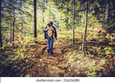 A mother is hiking on a trail in a forest with her baby in a back carrier during the autumn season.  Filtered to give retro, faded look. 