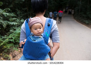 Mother Hold Baby Girl 10 Months On Back In Baby Carrier Walking In Waterfall Canyon. Travel Adventure And Hiking Activity With Child, Active And Healthy Lifestyle On Family Summer Vacation And Weekend