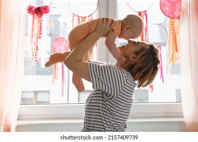 Mother holding baby in the air over decorated with Dreamcatchers sunny window at home. Happy woman playing with infant on sunlight. Positive future, motherhood. Copy space - Powered by Shutterstock