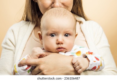 Mother Holding A Baby In Her Arms And Kissing It Studio Shot On Beige Background