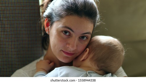 Mother Holding Baby Smiling To Camera. Real Life Authentic Casual Mom Looking To Camera Holding Sleeping Infant