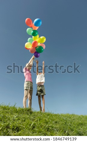 Mother holding a bunch of colorful balloons high enough to tease her daughter as she tries to reach them