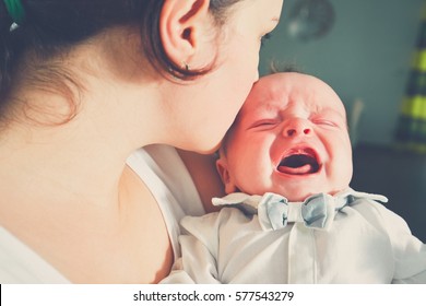 Mother holding crying baby. Young woman with her little son. 