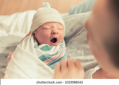 Mother holding cute newborn baby boy in her arms. Sleepy baby yawning.
