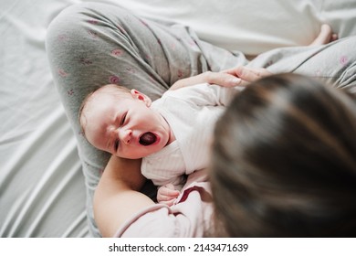 mother holding cute newborn baby girl yawning at home. Family concept