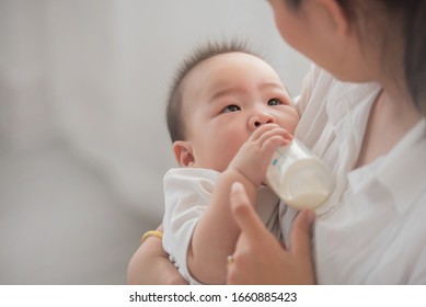 mother holding and feeding baby from milk bottle.portrait of cute baby being fed by her mother using bottle. loving woman giving drink milk to her son. mother feeding newborn baby from bottle at home