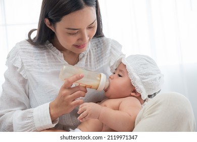 Mother holding and feeding baby from milk bottle at home. Portrait of cute newborn baby being fed by her mother using bottle. woman giving to drink milk to her son. Alternative to breast feeding.