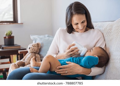 Mother holding and feeding baby from milk bottle. Portrait of cute newborn baby being fed by her mother using bottle. Loving woman giving to drink milk to her son.