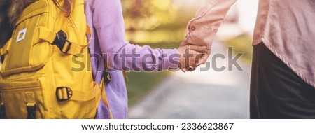Mother holding the hand of a daughter and escorting her to school.