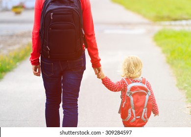 Mother holding hand of little daughter with backpack going to school or daycare