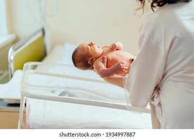 Mother holding hands, calming down, nursing, putting her infant baby in hospital bed in postpartum ward. Baby health care concept.