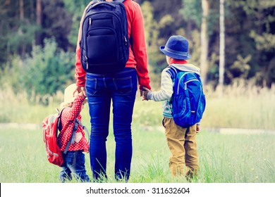 Mother Holding Hands Of Two Kids With Backpack Going To School Or Daycare