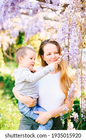 Mother is holding her 6-year old in her arms and showing him wysteria tree