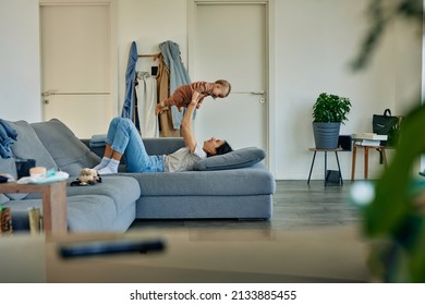 Mother Holding Up Her Baby While Lying On Her Sofa At Home