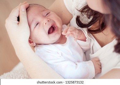Mother holding her crying little baby. and checks forehead. Newborn baby is crying in mom's arms.