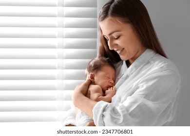 Mother holding her cute newborn baby indoors. Space for text - Powered by Shutterstock