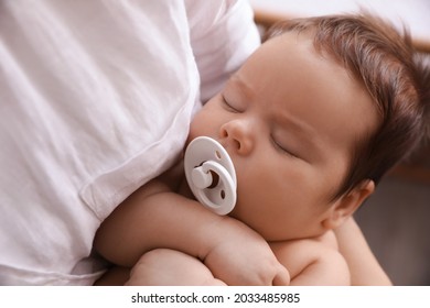 Mother holding her cute sleeping baby with pacifier on blurred background, closeup