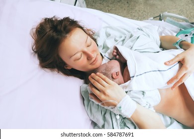 Mother holding her newborn baby child after labor in a hospital. Mother giving birth to a baby boy. Parent and infant first moments of bonding. - Shutterstock ID 584787691