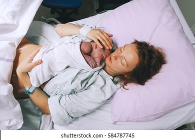 Mother holding her newborn baby child after labor in a hospital. Mother giving birth to a baby boy. Parent and infant first moments of bonding.