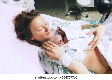 Mother Holding Her Newborn Baby Child After Labor In A Hospital. Mother Giving Birth To A Baby Boy. Parent And Infant First Moments Of Bonding.