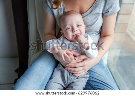 Mother holding her newborn child. Woman and new born boy relax near the windiow. Mother breast feeding baby. Family at home. Young mother playing whith her newborn son