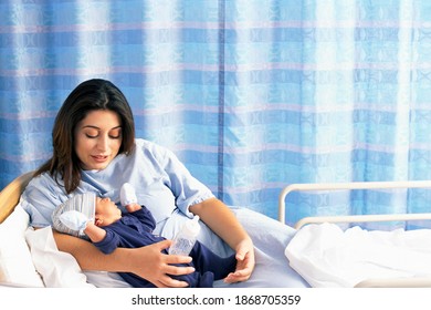 A mother holding her sleepy baby son with complete care while lying on a hospital bed - Powered by Shutterstock