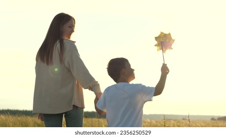 mother holding her son hand at sunset park. happy family walk children with mom summer park. chidhood dream. windmill hand small child sunset. children toy. kid holding hand matter. happy family.