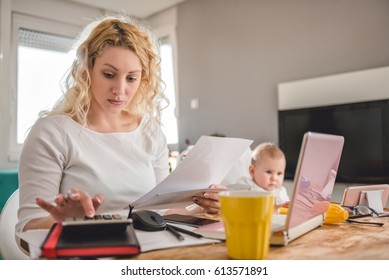 Mother Holding Letter And Using Calculator At Home Office And Taking Care Of Her Baby