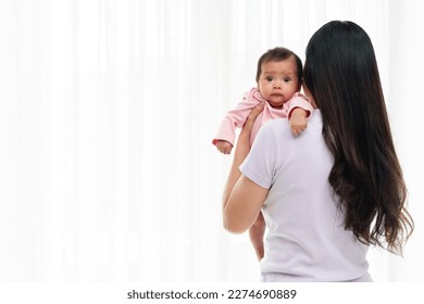 mother holding newborn baby burping after feeding milk on white window background