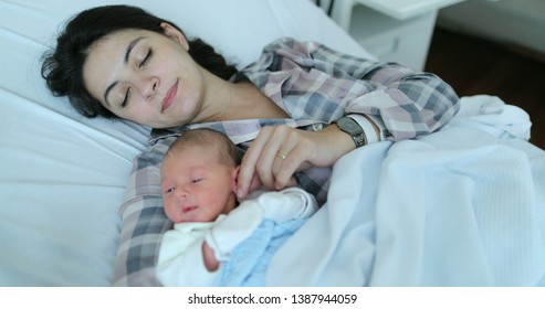 Mother holding newborn baby falling asleep together at hospital after birth in bed
